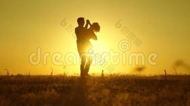 爸爸心爱的孩子在她的怀里跳舞，在飞翔，笑。 快乐的婴儿在日落时和他的父亲玩。 一张剪影